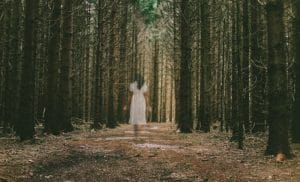 a woman, in white, walking in the forest of unforgiveness looking for God and forgiveness.